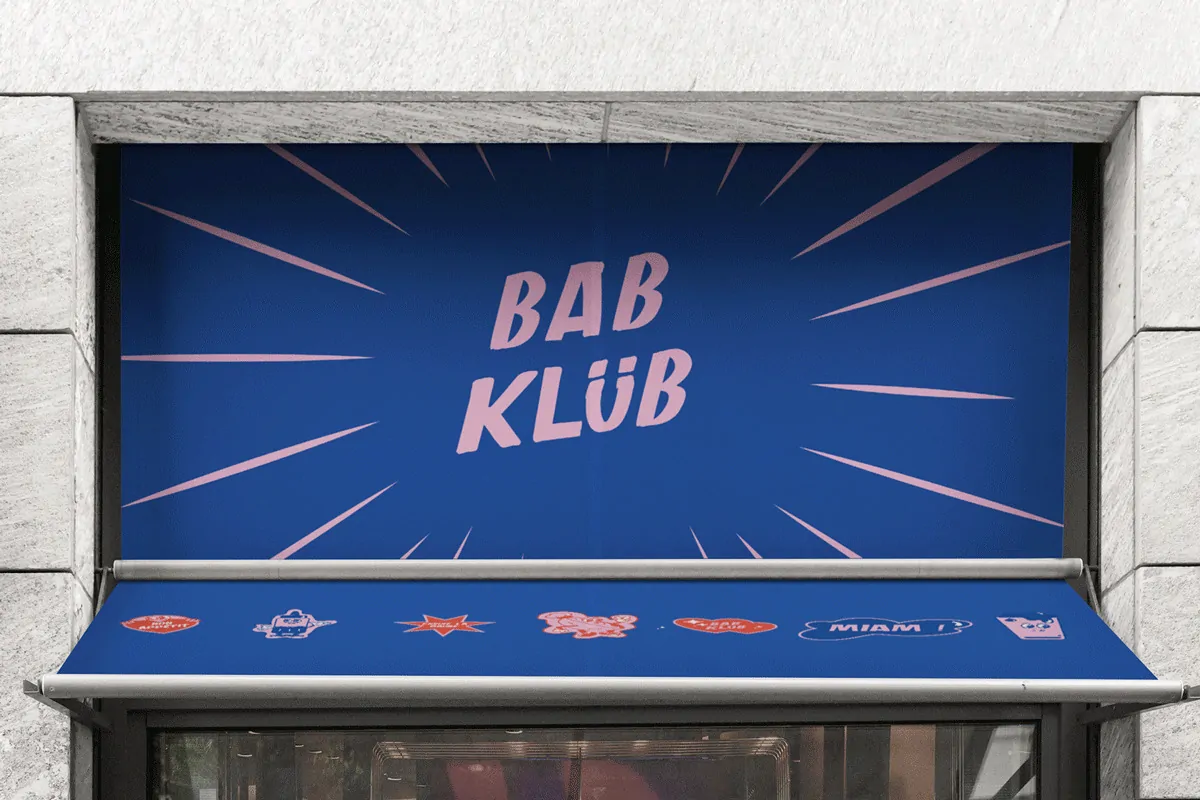 Le store d’une devanture de commerce imprimé du logo « Bab Klüb » en rose sur fond bleu.