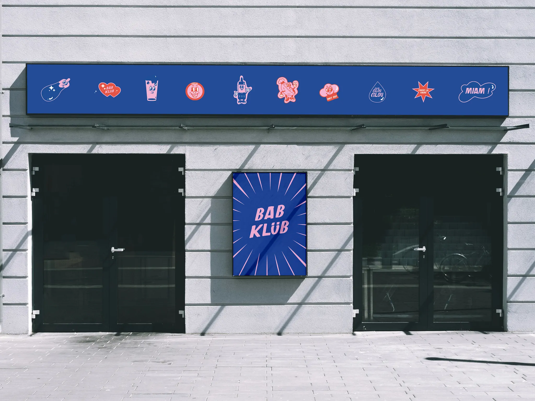 Une façade grise : une enseigne bleue ornée d’autocollants et un panneau carré « Bab Klüb » entre deux vitrines noires.