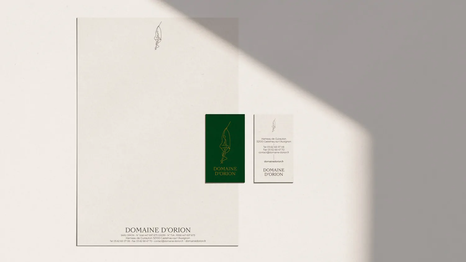 Un papier à en-tête, une carte de visite verte et une carte crème posés sur un fond clair.