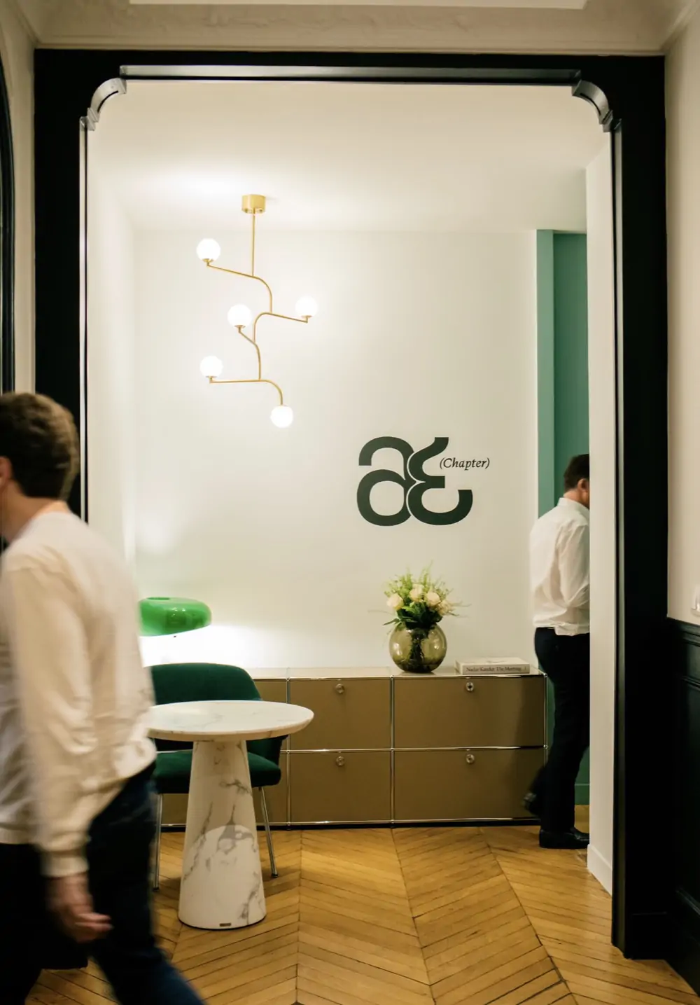 Chapter Avocats — le monogramme « æ (Chapter) » sur le mur blanc d’un bureau, au fond d’un couloir parqueté